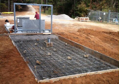 Rebar-grid concrete pump station pad on a red-clay job site