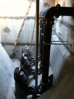 Wet-well interior with vertical pipe, chains, and submersible pumps